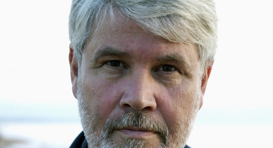 A pale-skinned man with gray hair and a beard, wearing a black shirt.