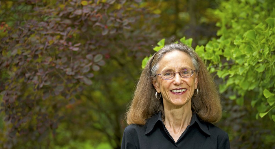 Woman with glasses standing in front of trees. 