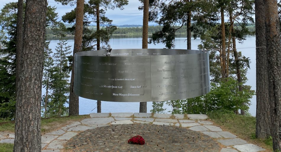 A metal memorial in the woods with a lake in the background.
