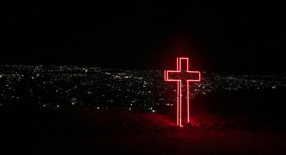 Rødt neonkors foran mørklagt by