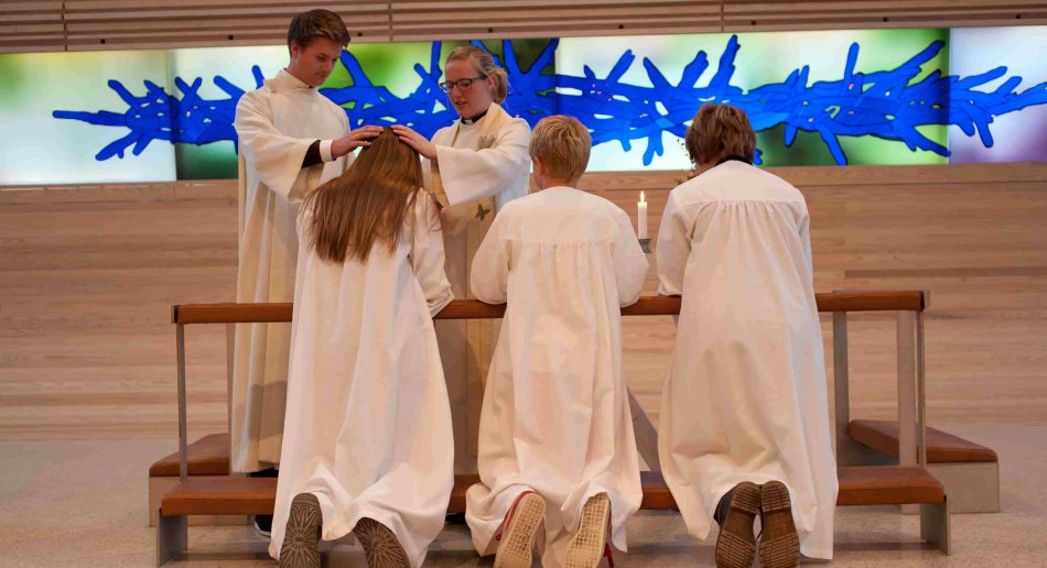 konfirmanter i hvite kapper som kneler ved alteret.