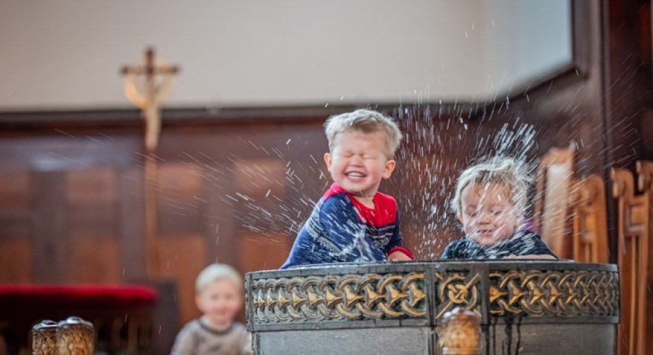 Barn som spruter med vann i døpefont i kirke