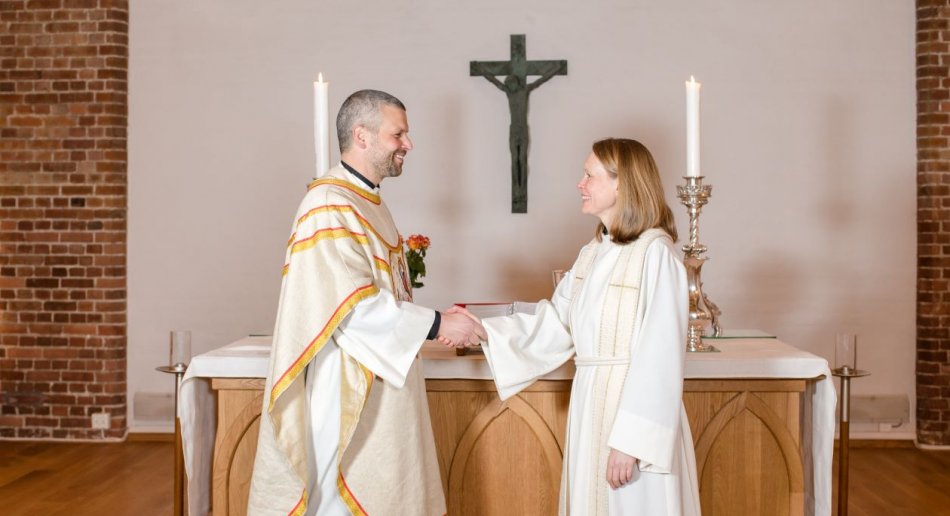 Prest og kateket som håndhilser foran alter i kirke