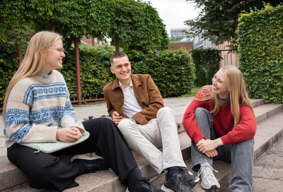 Tre studenter som sitter i en trapp ute.