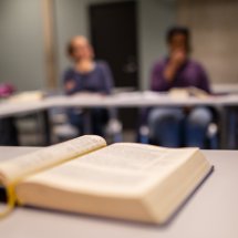 Oppslått bok i seminarrom med studenter