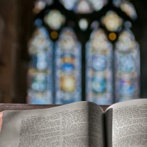 Oppslått Bibel foran vindu med glassmaleri